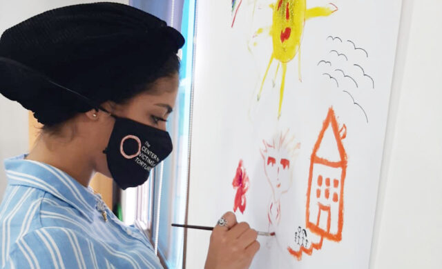 An individual wearing a face mask painting a simple picture.