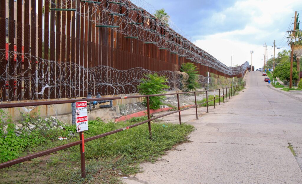 A tall fence with barbed wire at the bottom and top, the fence extends further than the horizon.