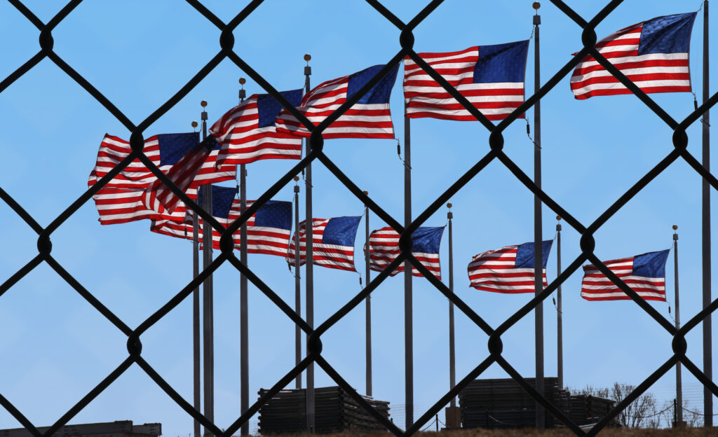 A wire fence with several American flags waving behind it.
