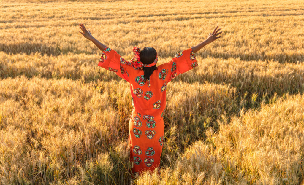 A woman stands in a golden field, arms partially raised.