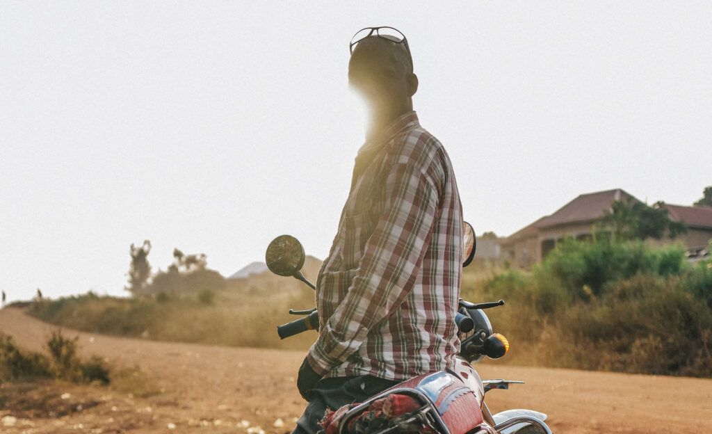 A man riding a motorcycle looks back at the camera, glare from the sun blocks most of the mans face.