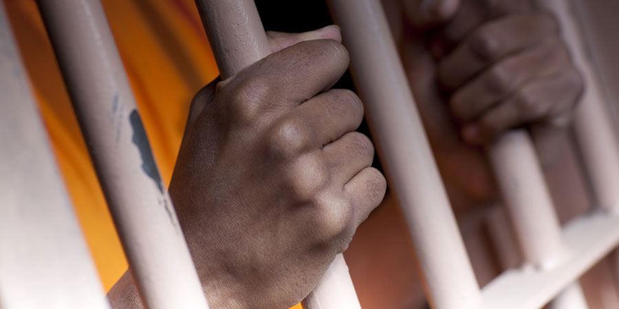 A man grips white prison cell bars.