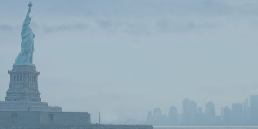 A side view of the Statue of Liberty, the New York city skyline just barely visible in the distance.