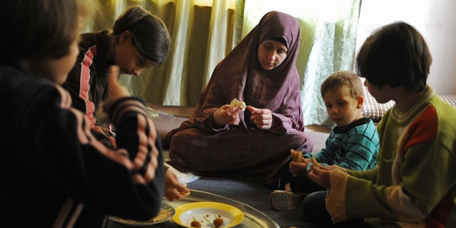 A woman and several children sit in a circle, eating food.