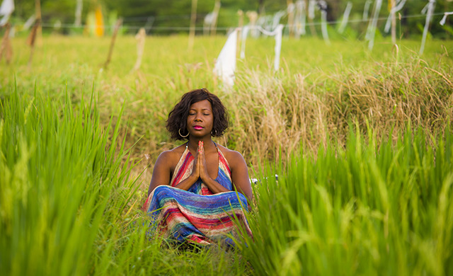 A woman in a field of grass sits meditating.