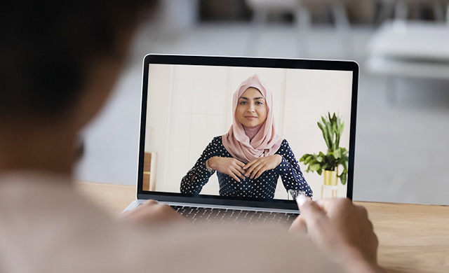 An individual video calls on a laptop with a woman in a hijab.